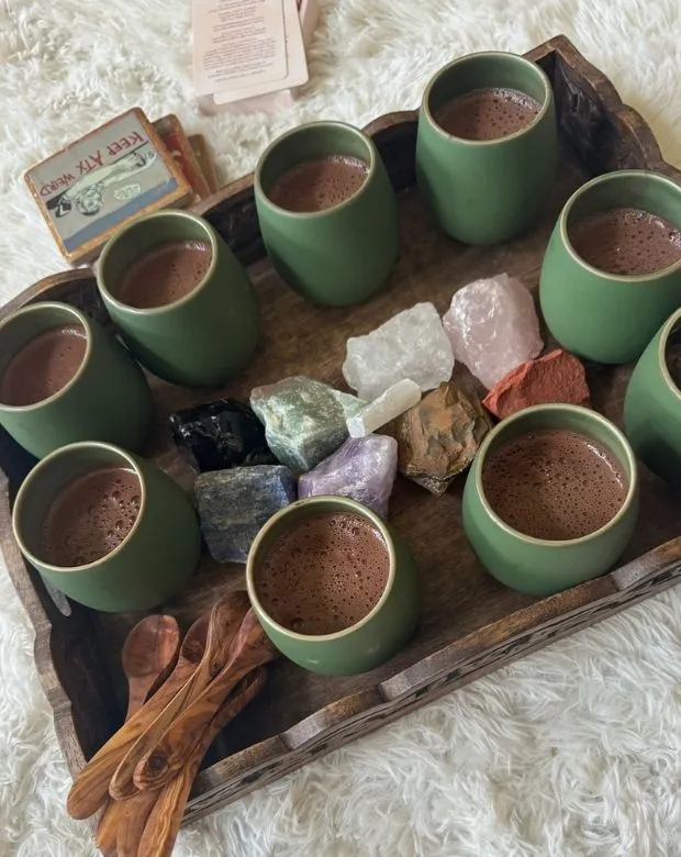 Cups of ceremonial cacao and small crystals arranged on a wooden tray